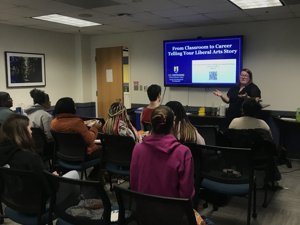 an instructor speaks to her students from the front of the class, with a screen behind her reading "from classroom to career: telling your liberal arts story"